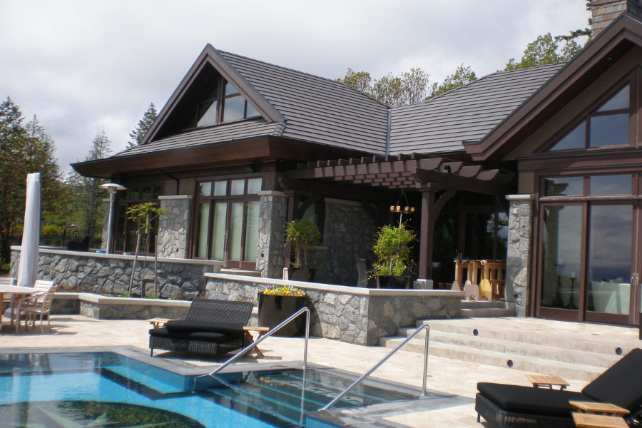 Contemporary Barrie Residence's backyard with a large stone patio, a beautifully tiled pool, stone features, and an arbor.