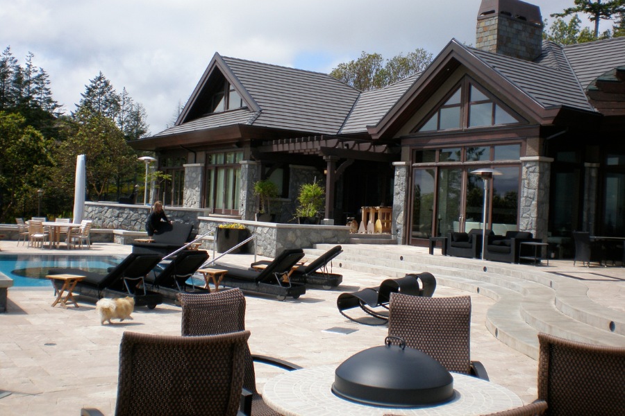 Contemporary Barrie Residence's backyard with a large stone patio, a beautifully tiled pool, outdoor seating, stone features, and an arbor.