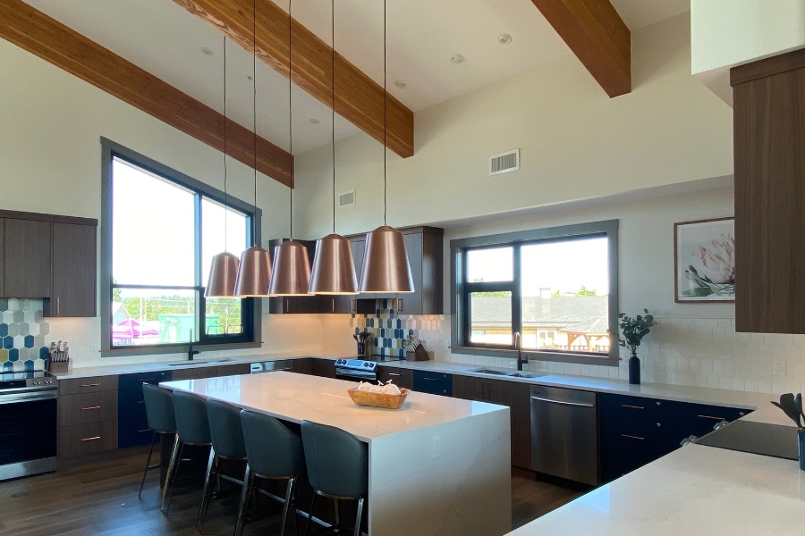 A kitchen with dark wood cabinets, beams on the angled ceiling, white countertops, and blue stools at the island, located in the Qwalayu House, designed by Alan Lowe Architecture.