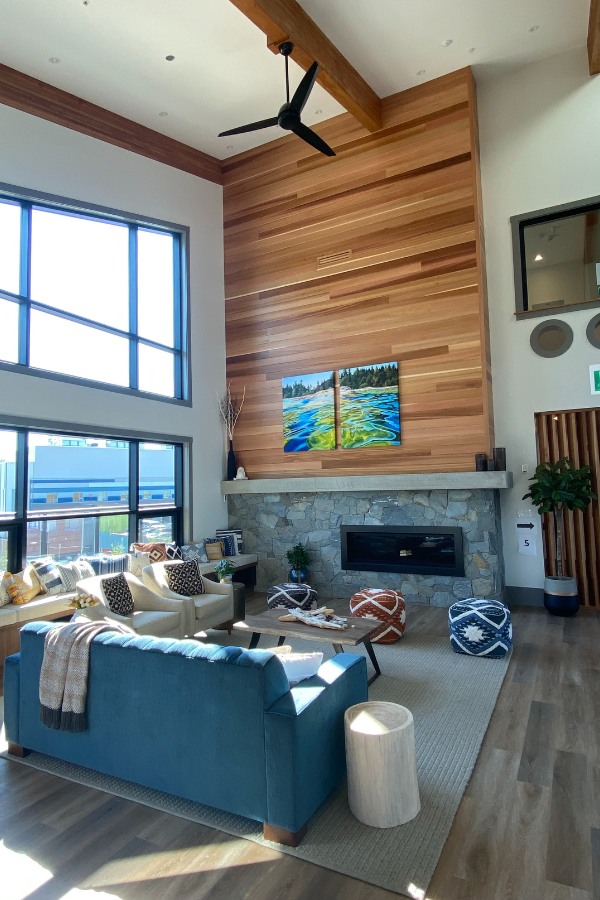 A living room with large windows, a stone fireplace with accents of wood, in the Qwalayu House, designed by Alan Lowe Architecture.