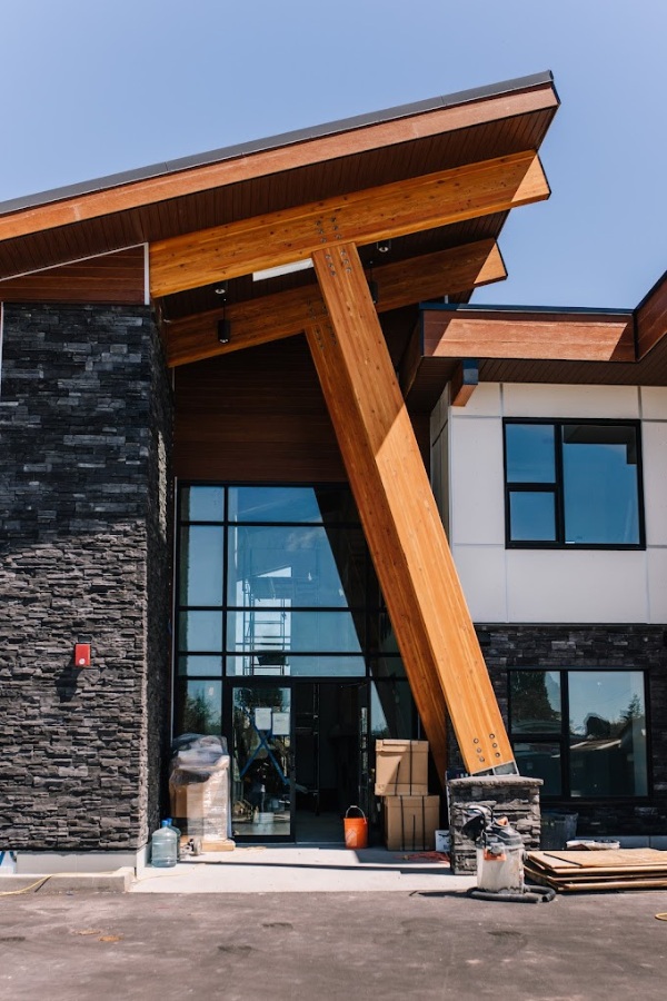 Modern Qwalayu House, designed by Alan Lowe Architecture, with an angled roof, stone and wood features, black trim and expansive windows.